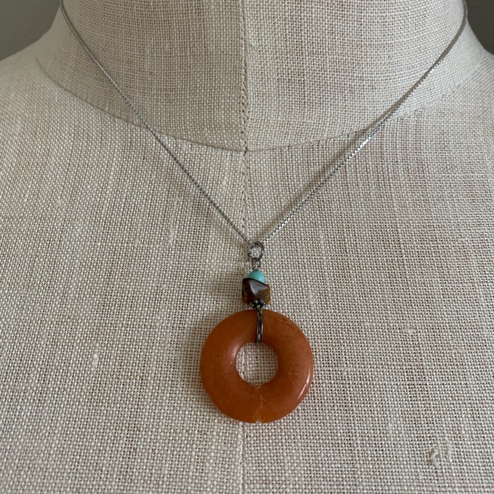 Pendant necklace with orange stone and silver chain.